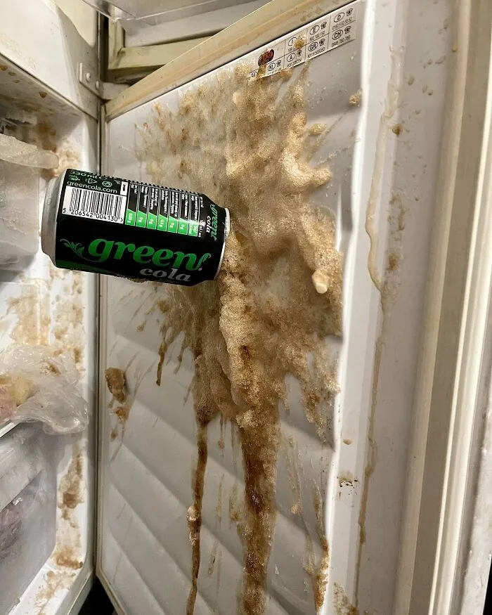 Exploded green cola can in freezer, frozen soda splattered on door, showcasing a random and cool mess.