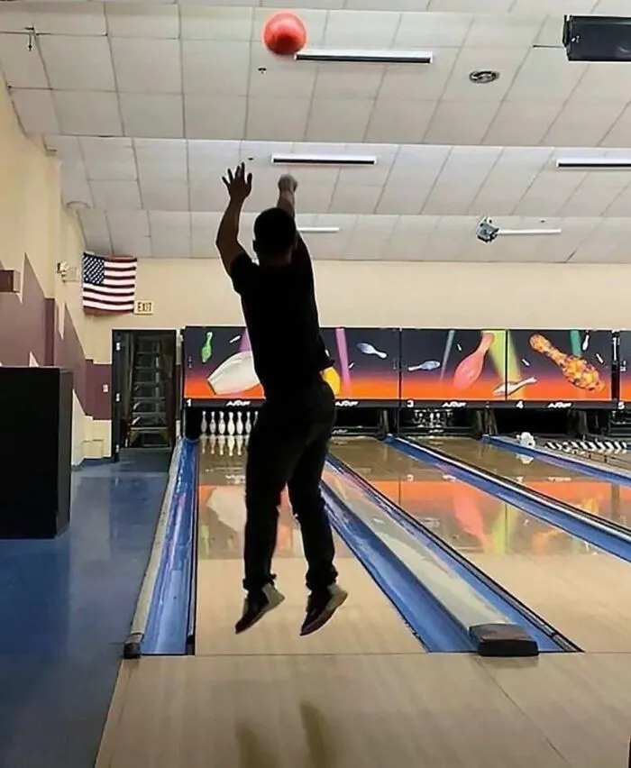 Person jumping to throw a bowling ball at a lane in an unusual pose that might make you uncomfortable.