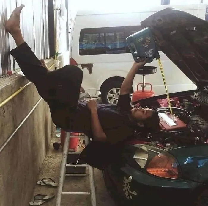 Man in an uncomfortable position pouring oil into a car engine, highlighting images that might make you uncomfortable.