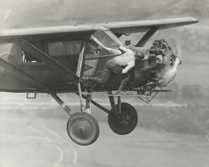 Man leaning out of vintage airplane engine during flight in an antique historical photograph showing early aviation technology.