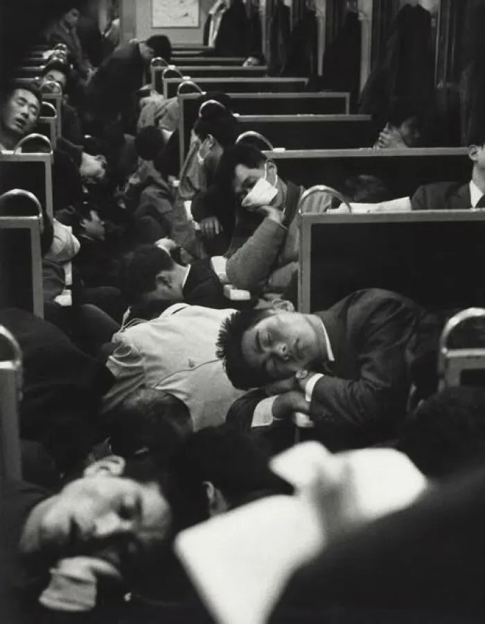 Crowded vintage train carriage with passengers sleeping and resting in an antique historical photograph depicting past daily life.