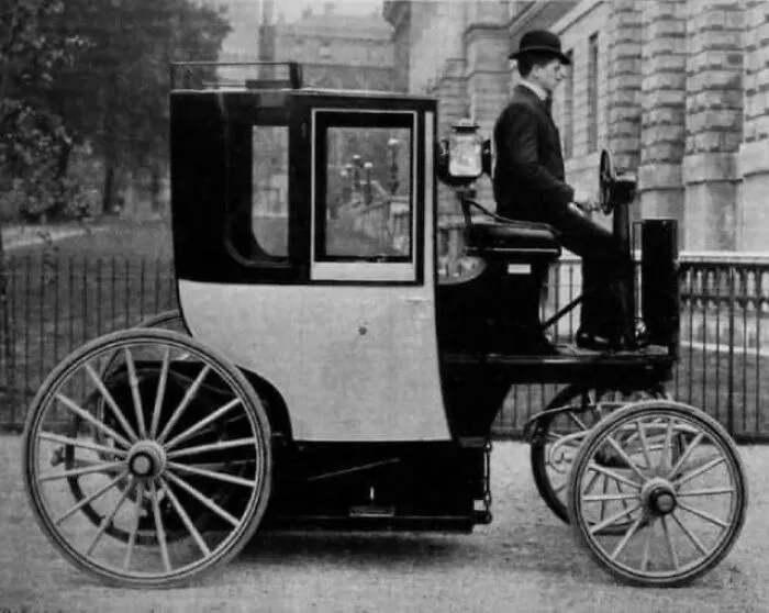 Early antique historical photograph showing a man in a bowler hat driving a vintage three-wheeled motor vehicle.