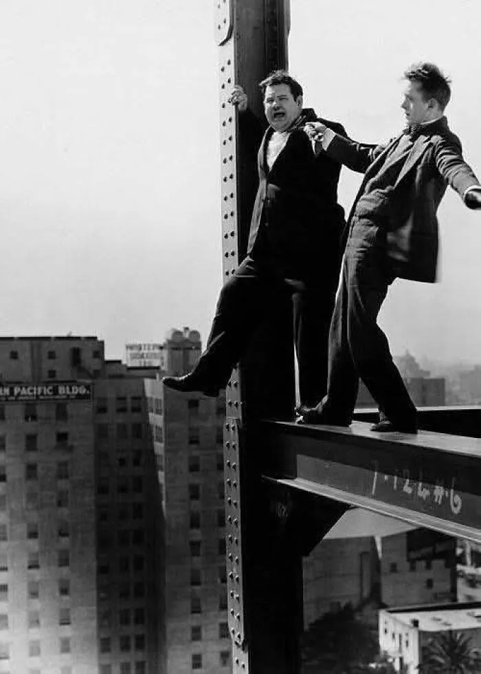 Two men balancing on a steel beam high above a city, an iconic antique historical photograph showcasing daring stunts.