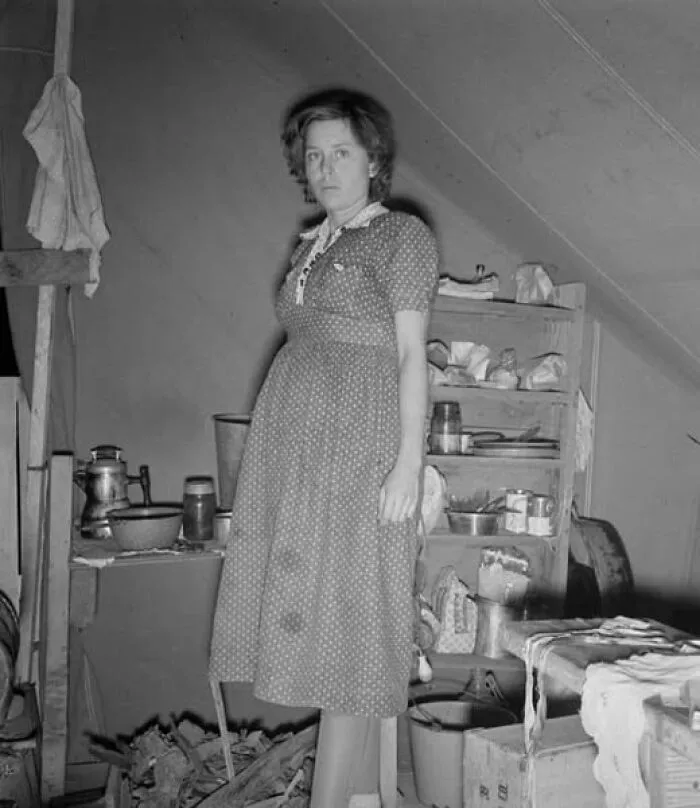 Woman in a vintage dress standing in a cluttered attic room in an antique historical photograph from the past.