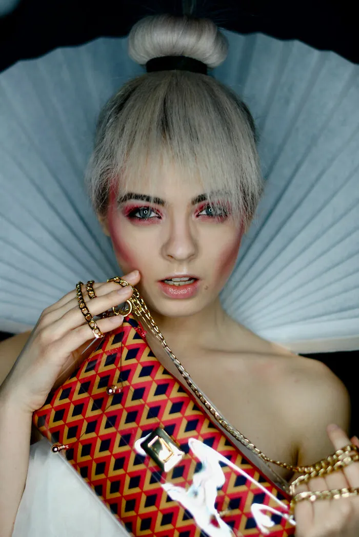 Young woman with bold makeup look and platinum hair bun holding a patterned handbag showcasing incredible makeup looks.