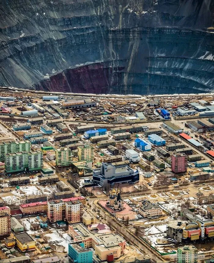 A massive open-pit mine towering over a small town, illustrating the scale of megalophobia with scarily big structures.