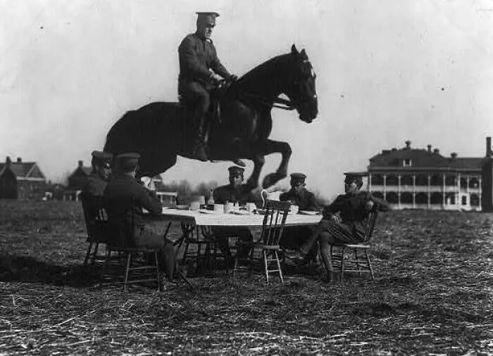 U.S. Army Men Seated Around Table, With One On Horseback Jumping Over The Table
