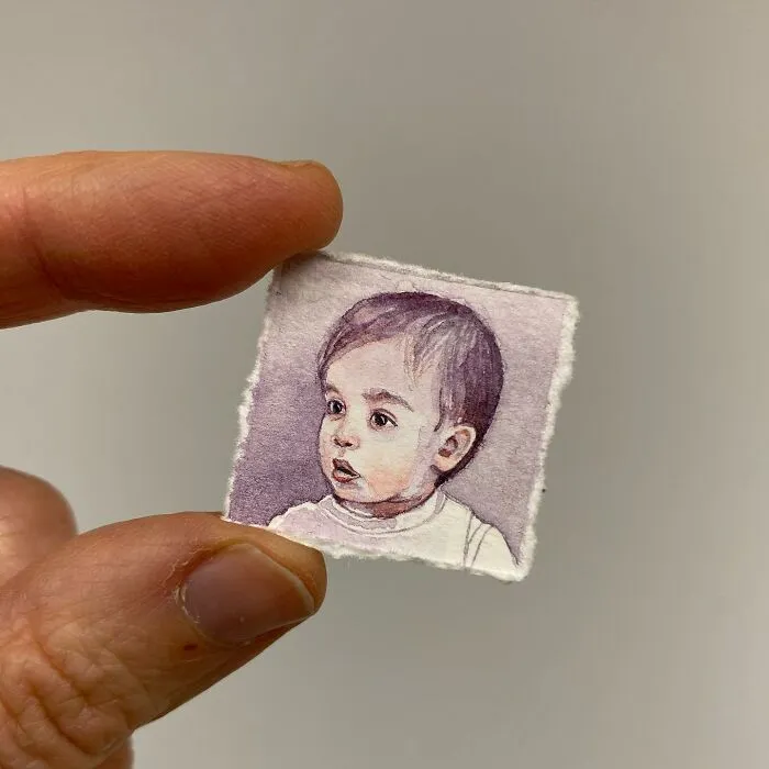 Hand holding a tiny one-inch painting of a baby’s portrait, showcasing detailed miniature artwork of everyday things.