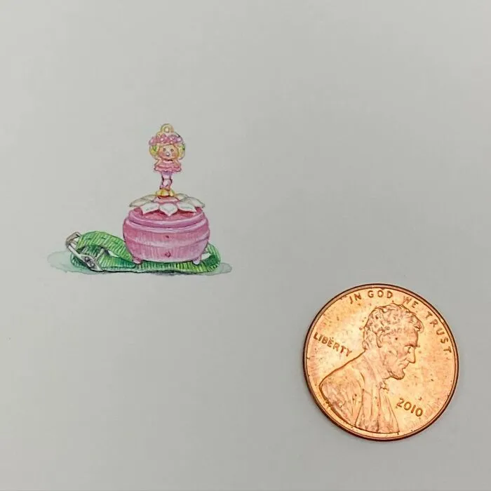 Tiny one-inch painting of a pink music box with a dancing figurine next to a US penny for size comparison.