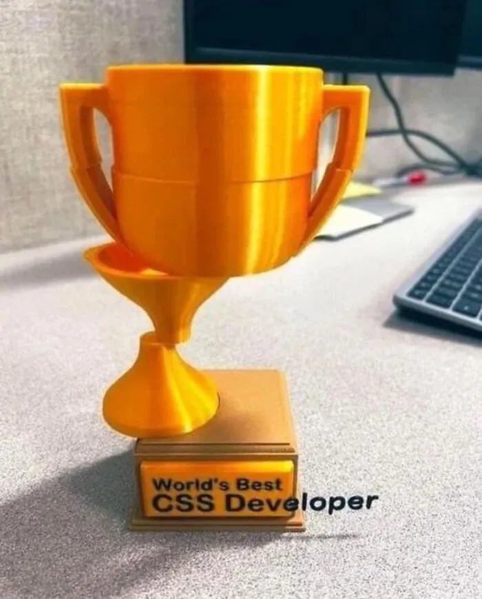 Trofeo dorado con diseño extraño, representando una imagen bendecida y maldita al mismo tiempo en un escritorio.