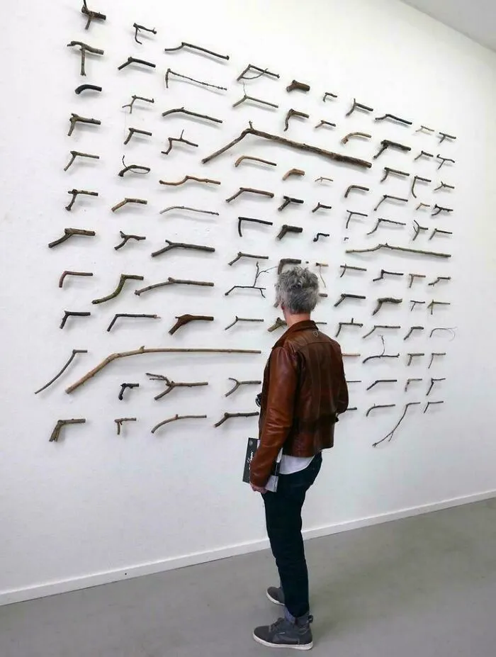 Persona observando una colección de ramas en la pared, imagen con elementos bendecidos y malditos al mismo tiempo.