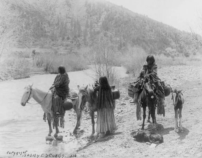 Three Apaches, One With A Child, With Horses Laden With Water Jugs, A Colt, And A Dog Stopped Beside A Stream