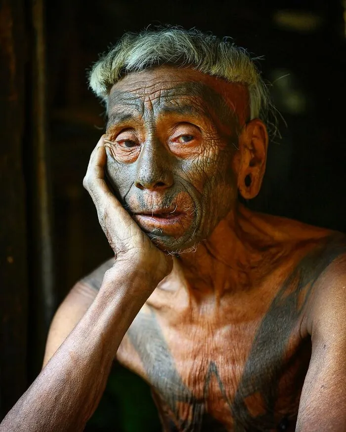 Retrato elocuente de persona mayor con tatuajes tradicionales, mostrando la sabiduría y cultura en su rostro.