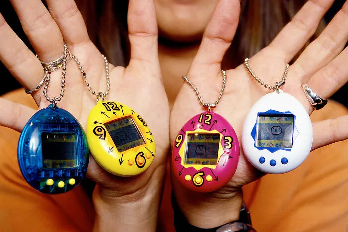Hands holding colorful virtual pets, a popular cringey nineties fashion accessory from the 90s era.