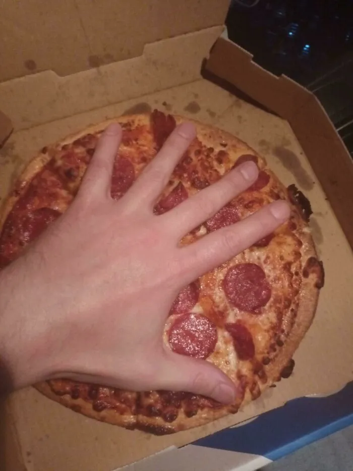 Hand placed over a small pepperoni pizza in a box showing products getting smaller and more expensive comparison.