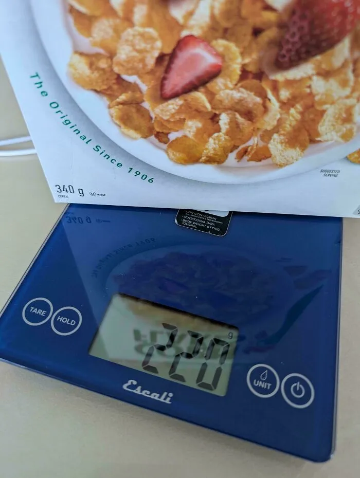 Box of cereal weighed on a kitchen scale showing a smaller product size compared to original packaging weight.