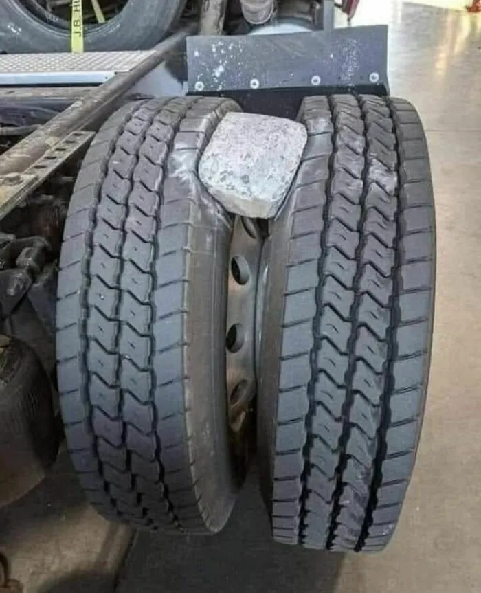 Truck tires showing an unexpected fail with a large rock stuck between the dual wheels causing damage and misalignment.
