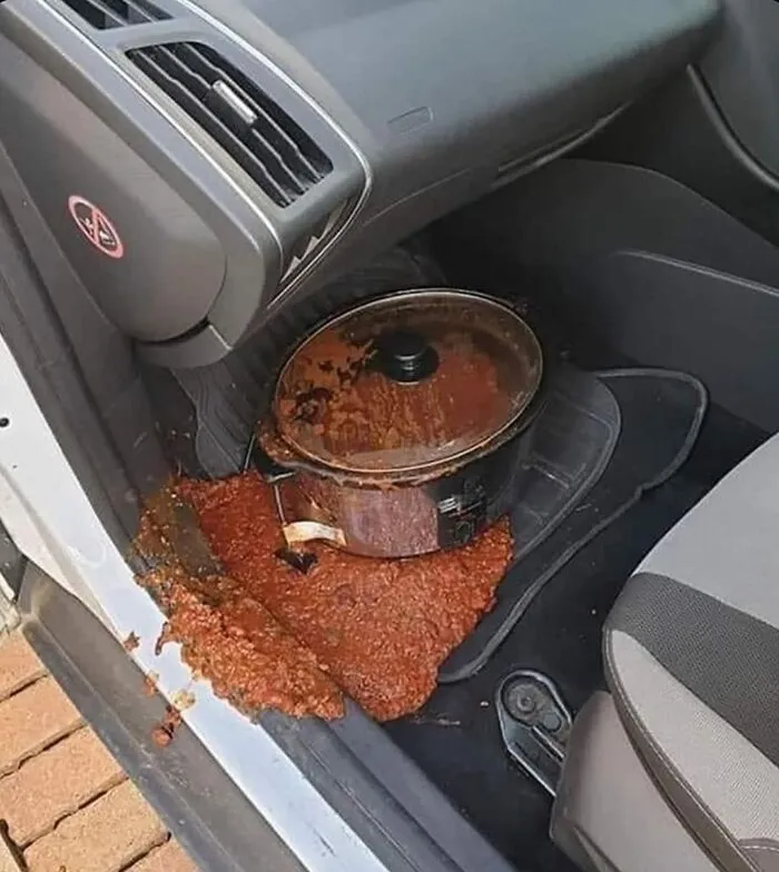 Pot of spilled food mess inside car on floor mat showing an unexpected fail in cooking gone wrong scene.