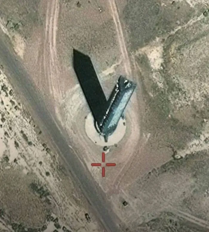 Vista aérea de un lugar raro encontrado en Google Earth con estructura que proyecta sombra alargada en terreno árido.