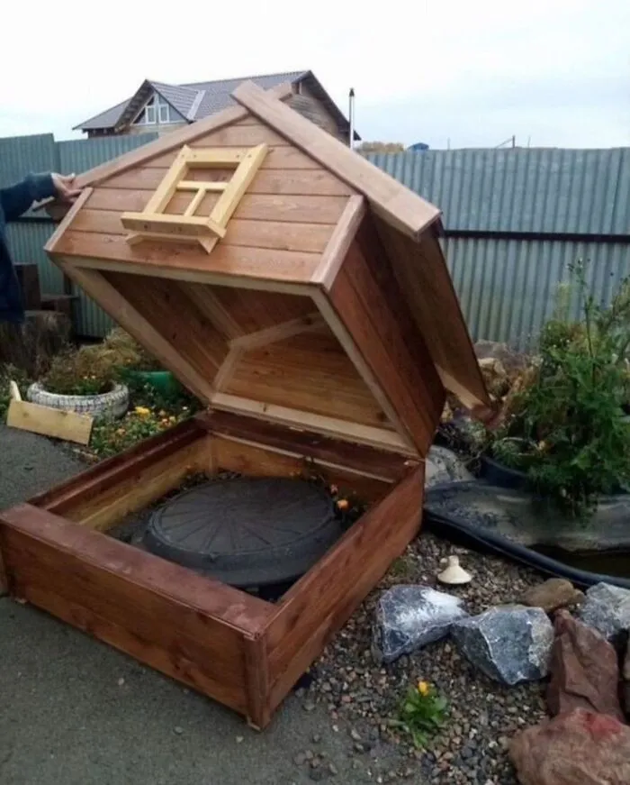 Woodworking ideas of a wooden storage box designed like a small house with a hinged roof lid outdoors.