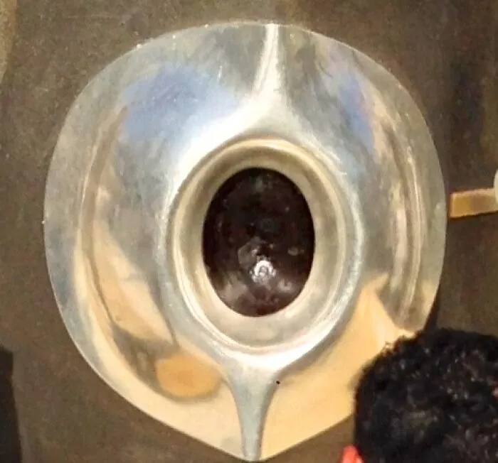 Silver medieval helmet with a dark oval visor, displayed as a bizarre historical artifact in a museum setting.