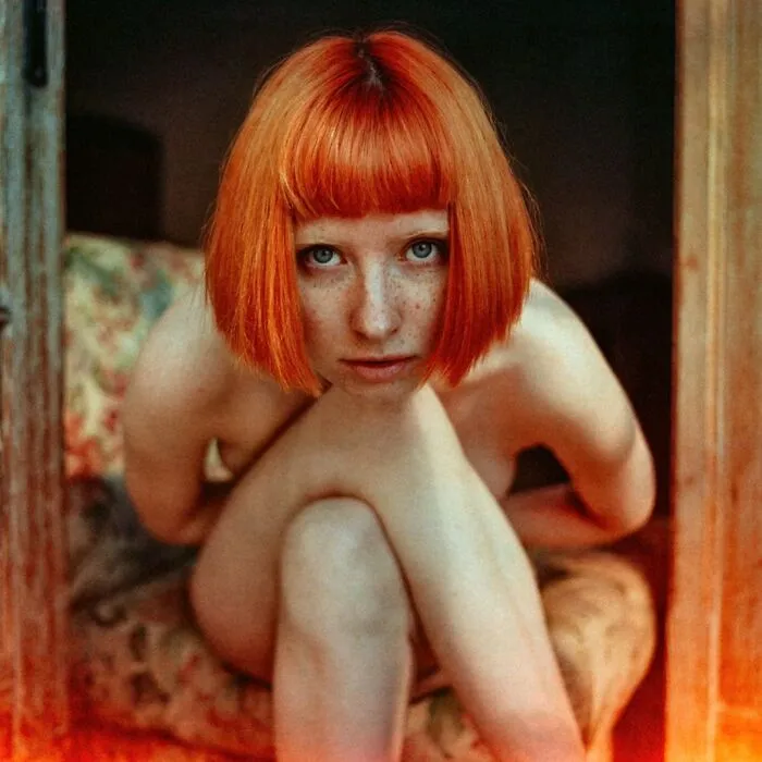 Young woman with red hair and freckles captured in an intimate, cinematic-looking shot by vintage camera photography.