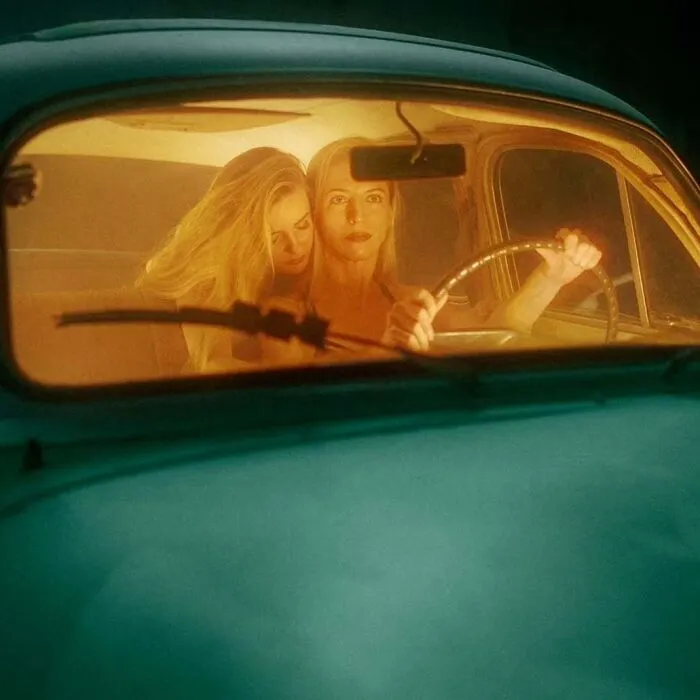Two women in a vintage car captured with vintage cameras creating intimate, cinematic-looking shots in warm lighting.