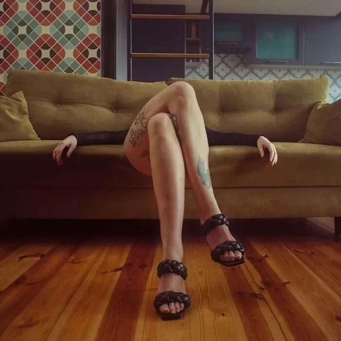 Person with tattoos reclining on a vintage-style sofa in a cinematic-looking shot, captured by a photographer using vintage cameras.