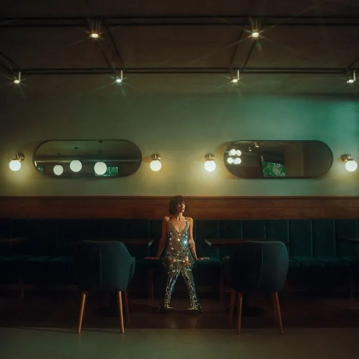 Woman in a shimmering dress sitting alone in a dimly lit room, shot with vintage cameras for cinematic-looking effect.
