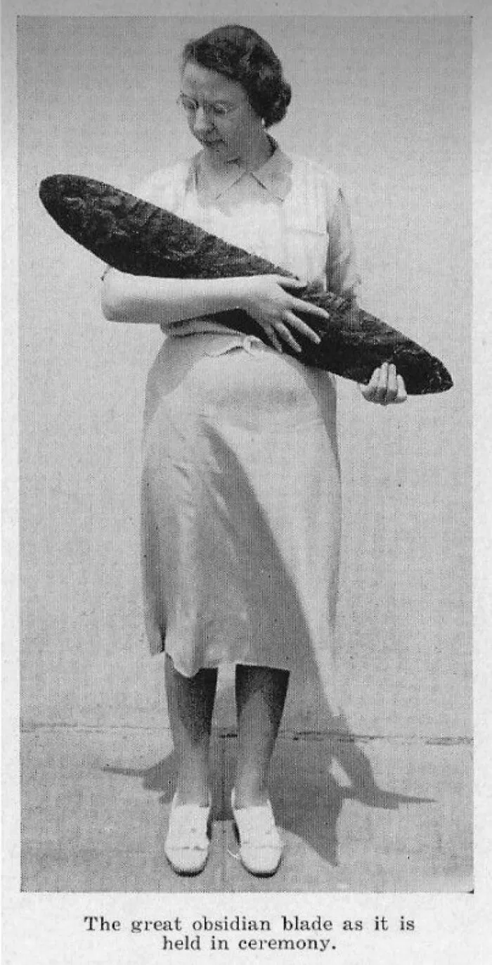 Woman holding a large obsidian blade, a bizarre historical artifact showcased in a black and white photo.