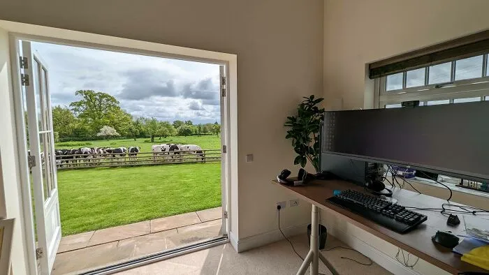 Home office setup with large monitor and keyboard facing an open door showing cows in a green pasture, work-from-home meme scene.