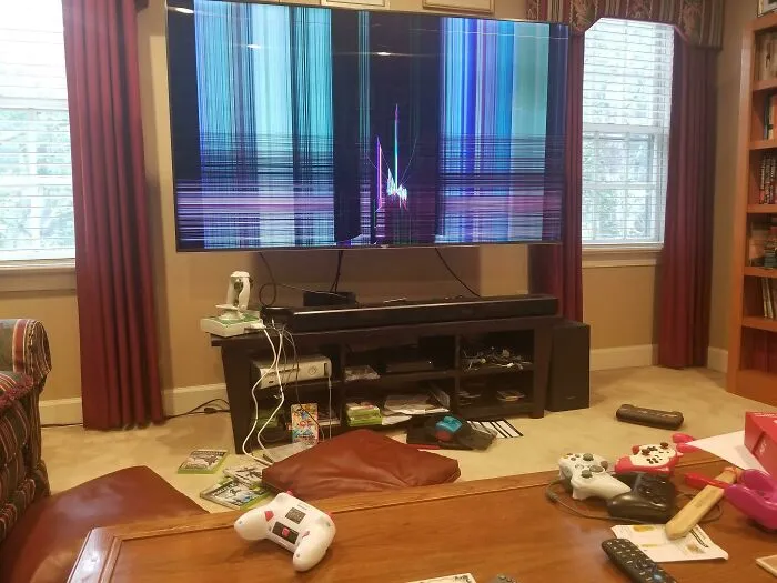 Televisor con pantalla rota en sala desordenada, mostrando un día peor para padres y madres en casa.