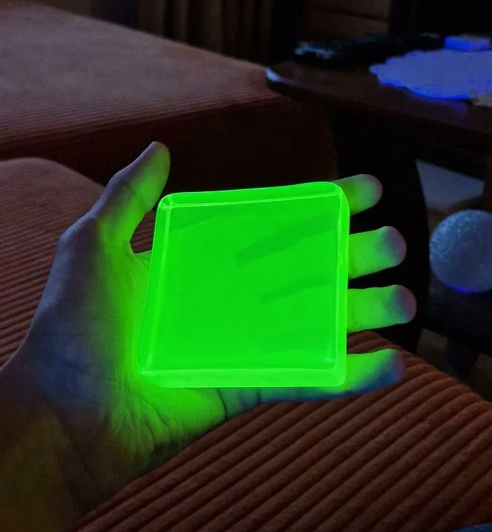 Mano sosteniendo un objeto cuadrado que emite luz verde brillante en un entorno oscuro, foto interesante para SEO.