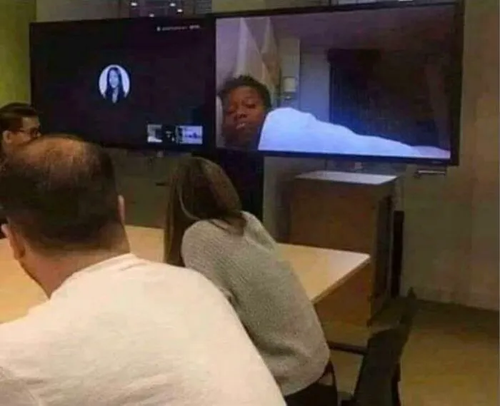 People attending a funny work-from-home video call with one participant lying in bed on the screen.
