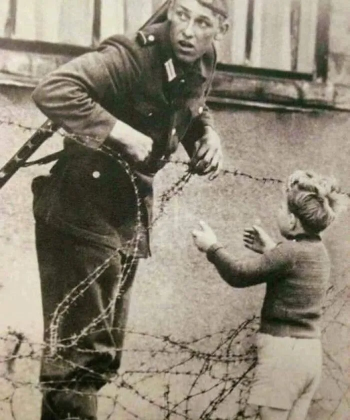 An East German Soldier Defying Orders To Help A Child Return To His Family After He Was Separated From Them When The Newly Erected Berlin Wall Was Built, 1961