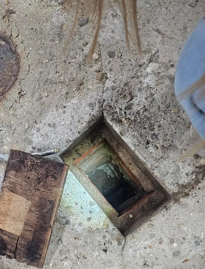 Square hidden trapdoor in old concrete floor revealing a dark, forgotten space in a home with a haunted past