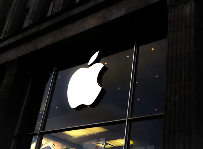 Apple store front with glowing logo at dusk, symbolizing former employees revealing disturbing workplace secrets.