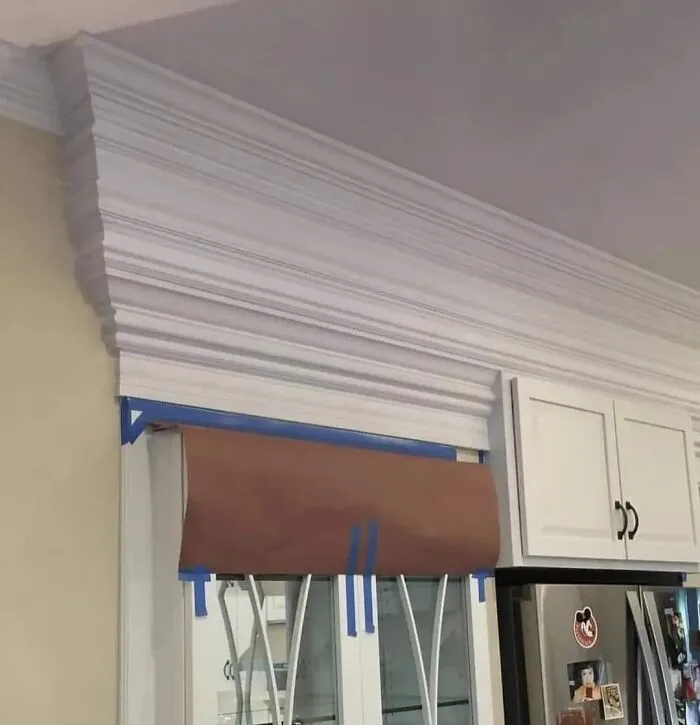 Poorly installed crown molding with taped paper covering glass cabinets showing renovation fails and saving mistakes.