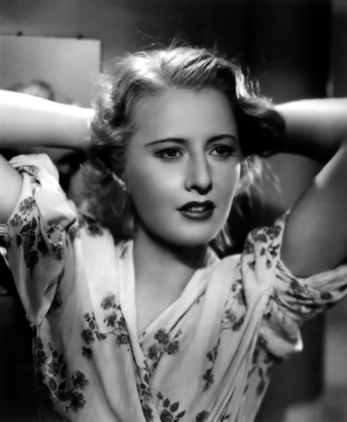 Black and white portrait of a glamorous 1940s Hollywood icon with vintage hairstyle and floral patterned dress.
