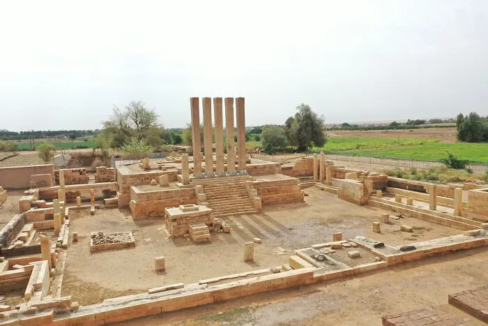 Ancient UNESCO treasure with tall stone pillars and ruins surrounded by green fields under a bright sky.