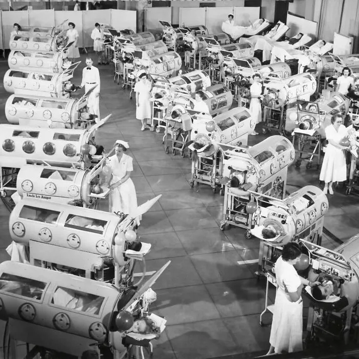 Sala de hospital con enfermeras atendiendo a pacientes en incuba doras médicas en fotografía histórica en blanco y negro.