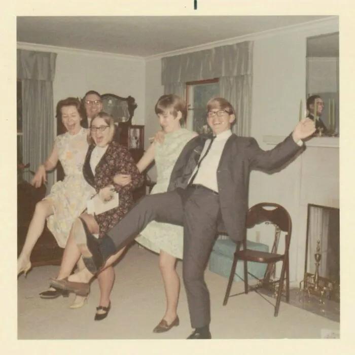 Group of four adults in vintage clothing dancing and having fun indoors in a mesmerizing vintage photo from history.