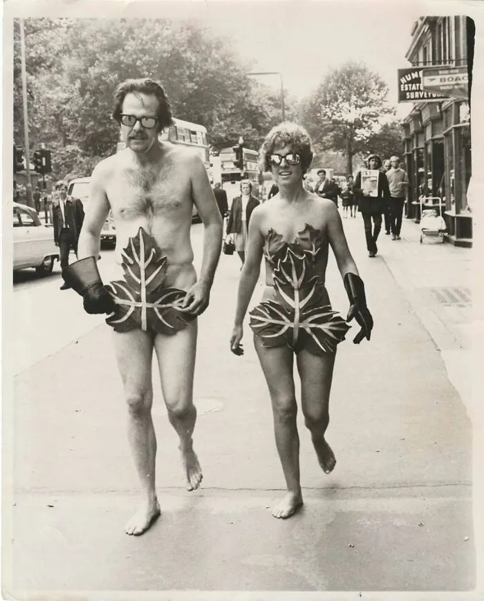 Vintage photo of a man and woman walking barefoot in leaf costumes on a city street, showcasing mesmerizing history.