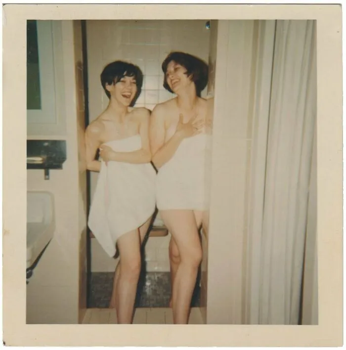 Two women wrapped in towels laughing together in a vintage photo capturing a candid moment from history.