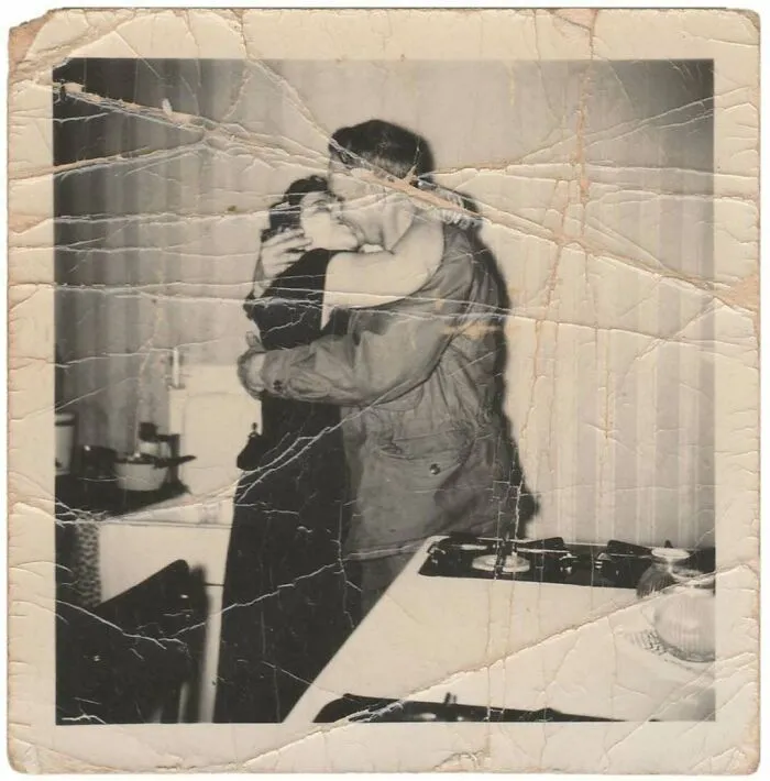 Vintage photo of a couple embracing and kissing in a kitchen showing a mesmerizing moment from history.