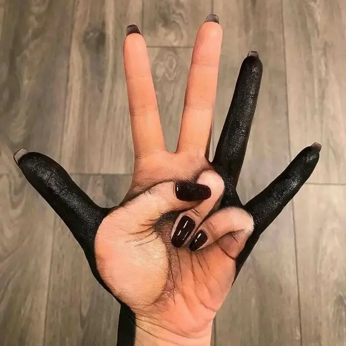 Mano con tatuaje creativo que combina espacio negativo y pintura negra, ejemplo de tatuajes que van de lo gracioso a lo terrible.