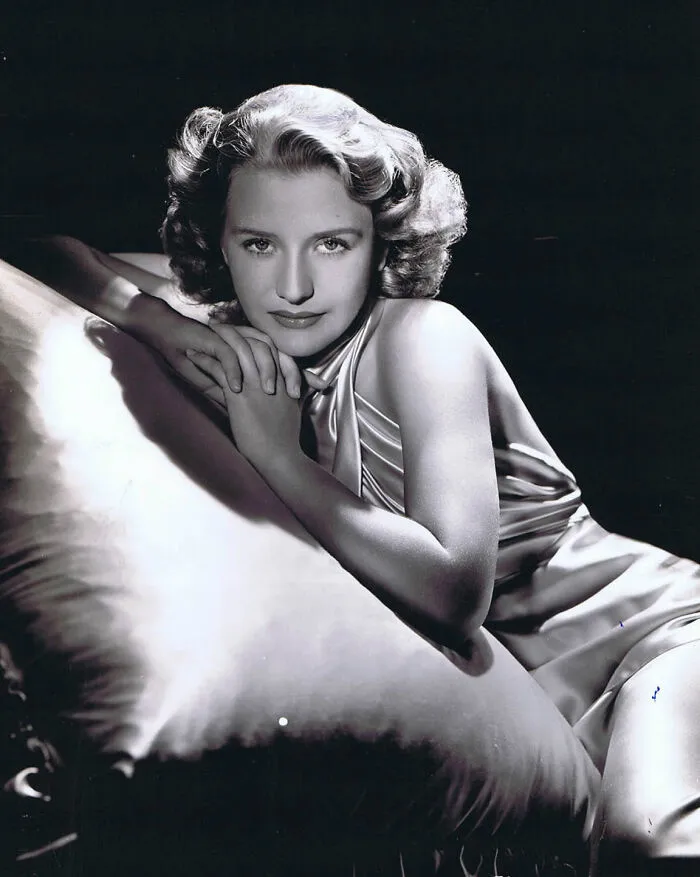 Black and white portrait of a glamorous 1940s icon reclining and posing in elegant vintage Hollywood style.