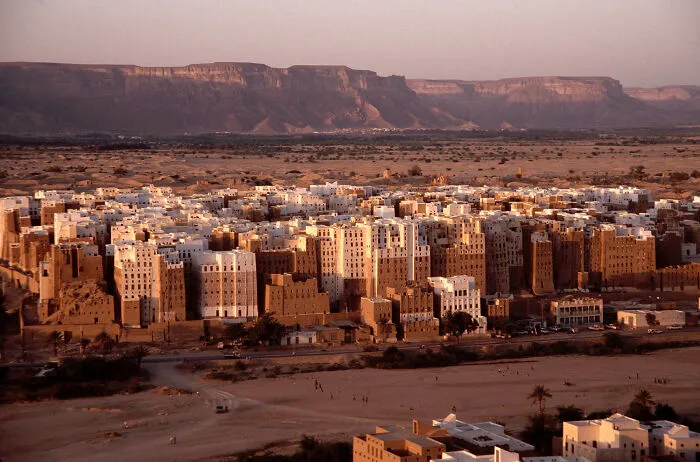 Ancient mudbrick buildings of a UNESCO treasure site set against a mountainous desert landscape at sunset.