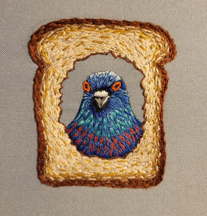 Colorful bird embroidered inside a slice of bread, showcasing beautiful embroidery designs with vibrant thread on fabric.