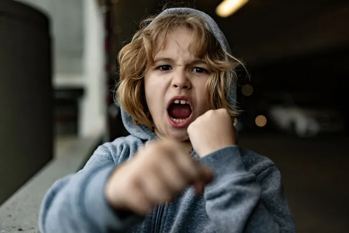 Young boy in a grey hoodie playfully pretending to punch, expressing fierce emotion in an urban setting, twins names theme.